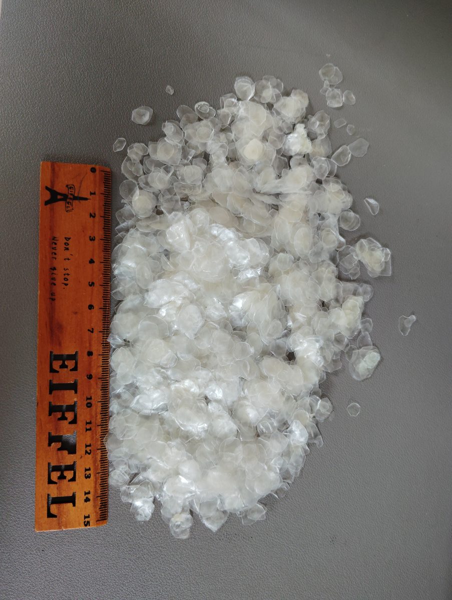 Demineralized tilapia fish scale flakes in a white dish beside a woven export bag on a light gray background