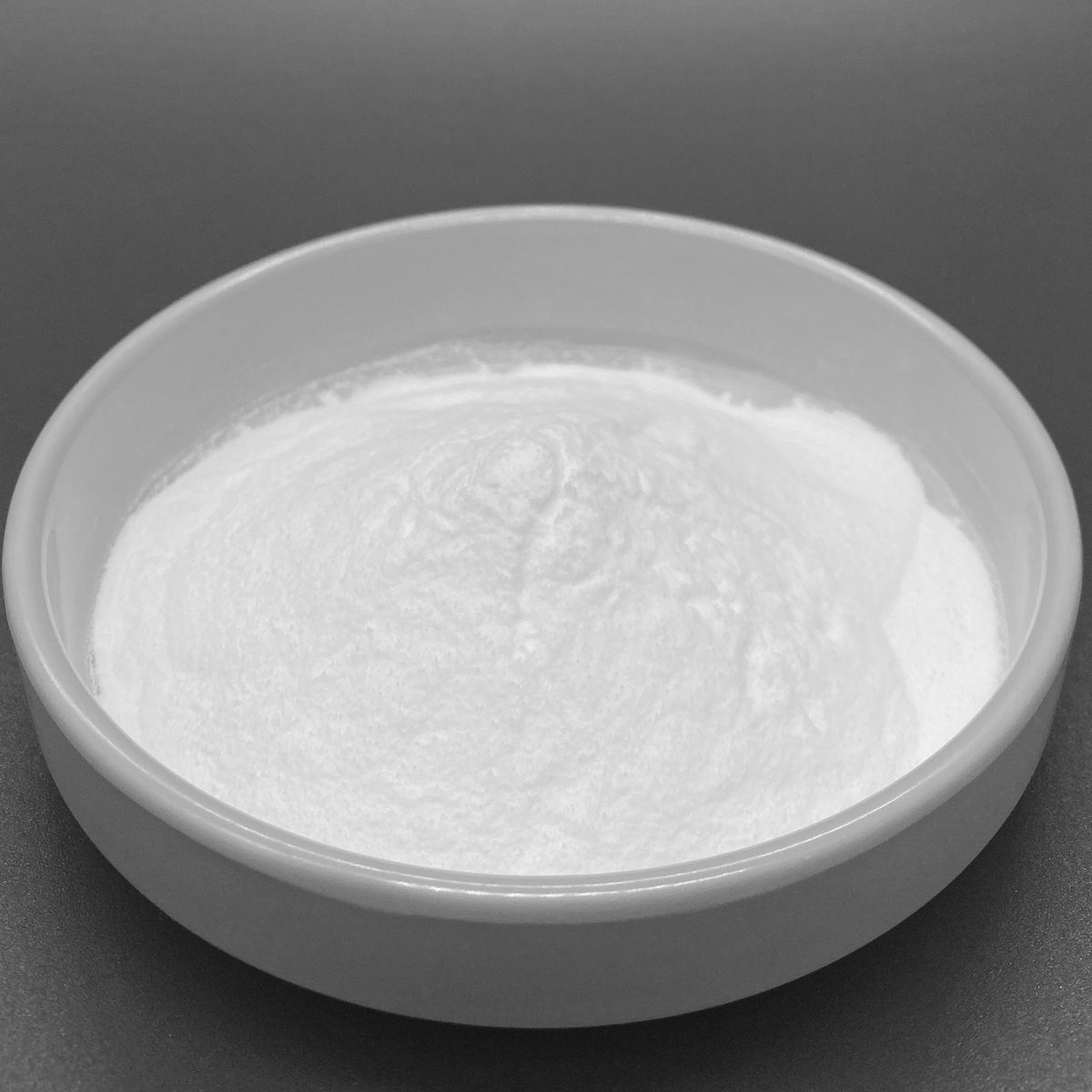 Fine white hydrolyzed fish collagen peptide powder in a dish with a stainless steel scoop on a light gray background